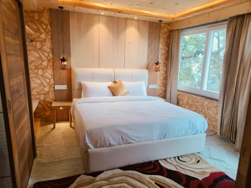 A warm wood-panelled suite bedroom with a king bed, pendant lamps and a bright window.